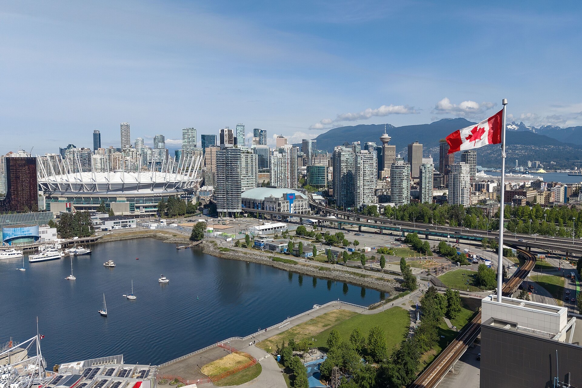 Vancouver downtown skyline seen across the water with the North Shore mountains behind and a Canadian flag in the foreground